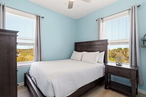 A bedroom with a bed, nightstands, a window with blinds, and a view of greenery. - Beach House - Salty Dolphin (Port St. Joe)