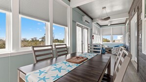 A dining area with a long table, chairs, and a view of the outdoors. - Beach House - Salty Dolphin (Port St. Joe)