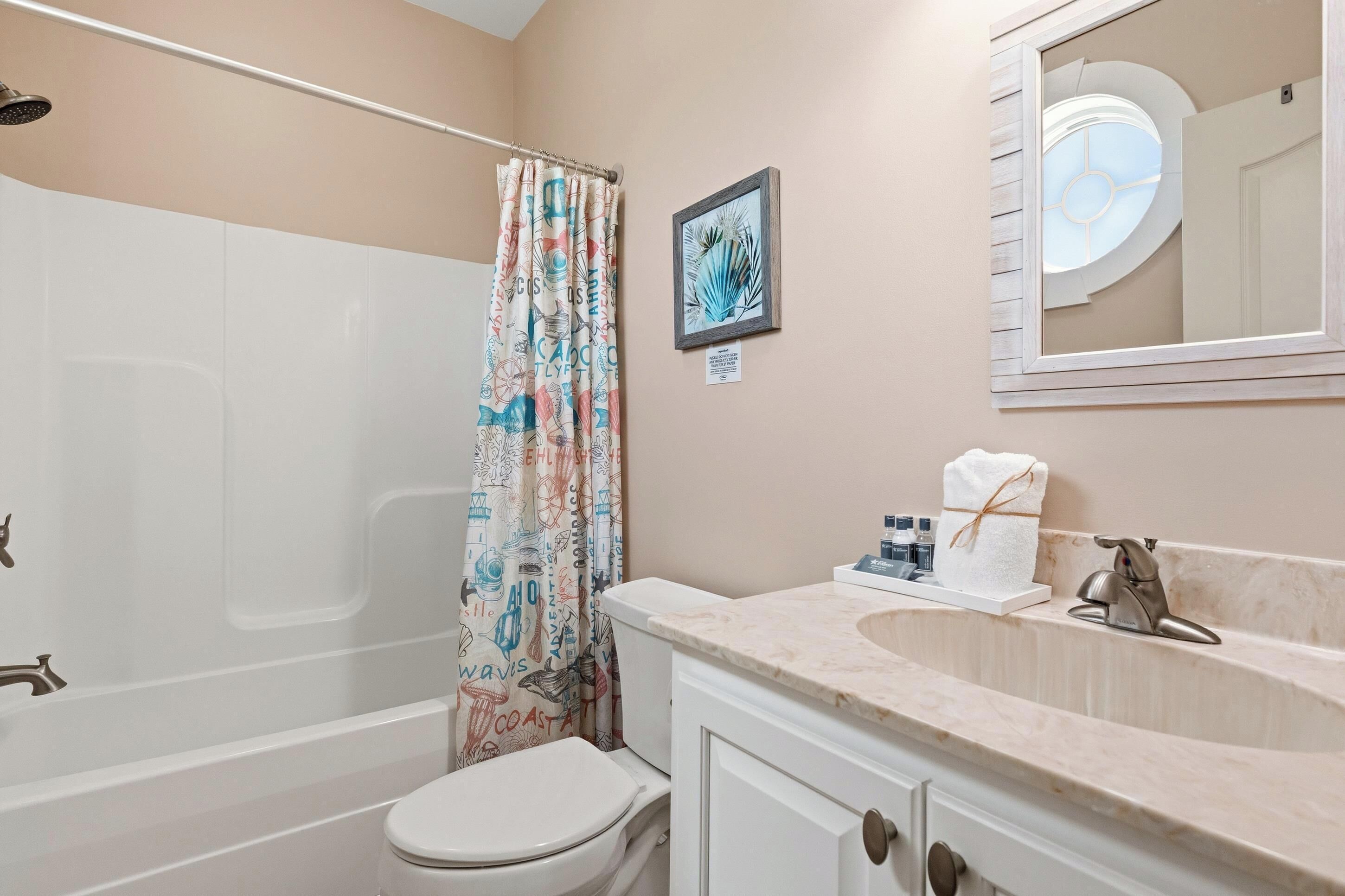 A bathroom with a shower, toilet, sink, and a framed picture on the wall.