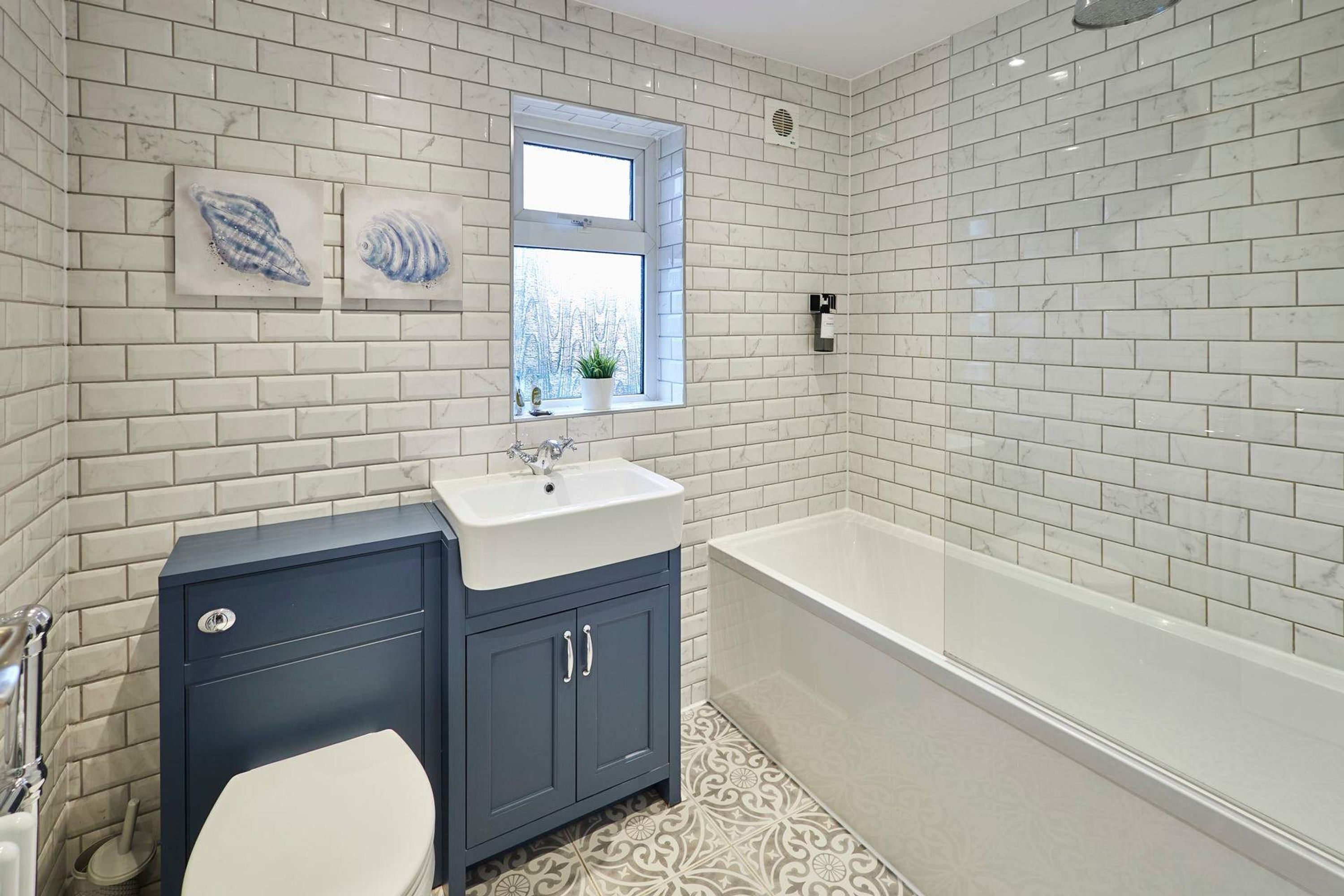 Une salle de bain avec des carreaux de marbre blanc, un meuble-lavabo bleu foncé, des toilettes blanches et une baignoire blanche.