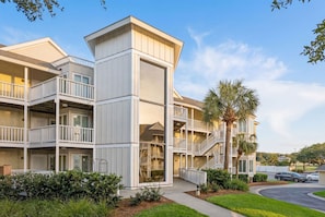A multi-story hotel with balconies, a central staircase, and a parking area. - Port O Call A202: Ocean View Condo in Wild Dunes (Isle of Palms)