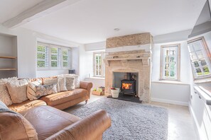Ein gemütliches Wohnzimmer mit Kamin aus Stein, einem braunen Ledersofa und einem großen Fenster mit Jalousien.