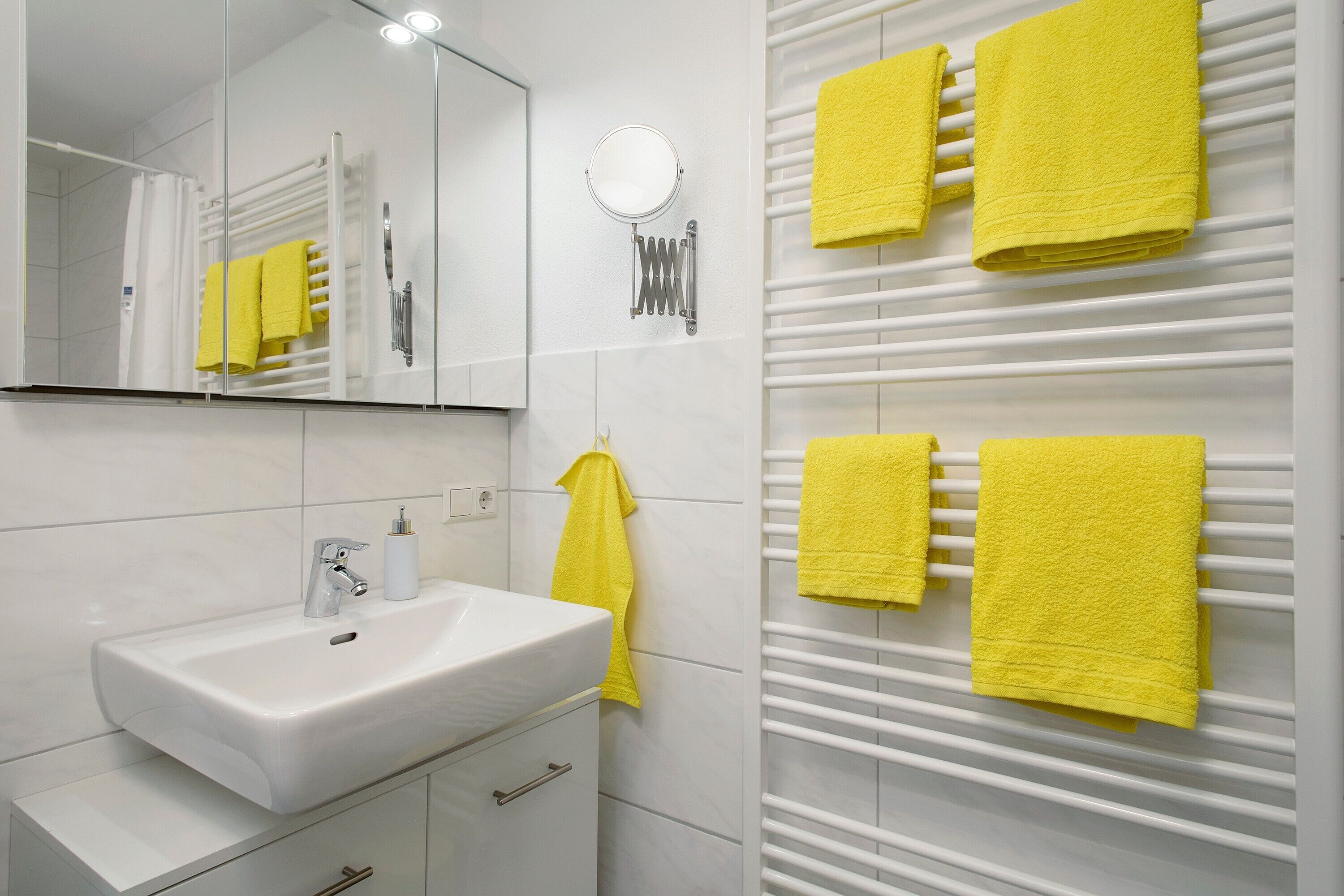 A bathroom with a white sink, mirror, and towel rack with yellow towels.