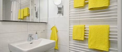 A bathroom with a white sink, mirror, and towel rack with yellow towels.