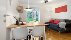 A modern living room with a dining table, chairs, a sofa with red cushions, a red abstract painting, and a view through a glass door. - Rieke's Apartment with Private Terrace and Wi-Fi (Friedrichshafen)