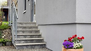 A concrete staircase leading to a building entrance, a metal handrail, and a flower planter with red, purple, and white flowers. - Rieke's Apartment with Private Terrace and Wi-Fi (Friedrichshafen)
