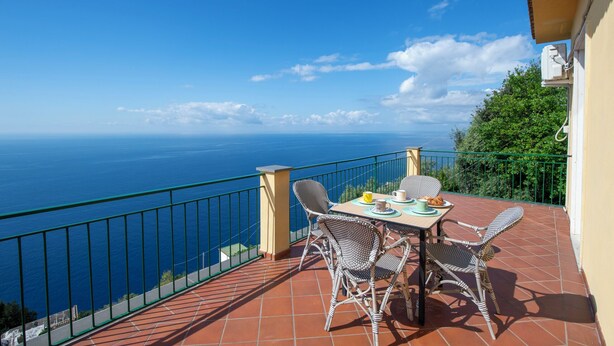 Un balcón con sillas de mimbre y una mesa dispuesta para dos, con vista a un paisaje marino.