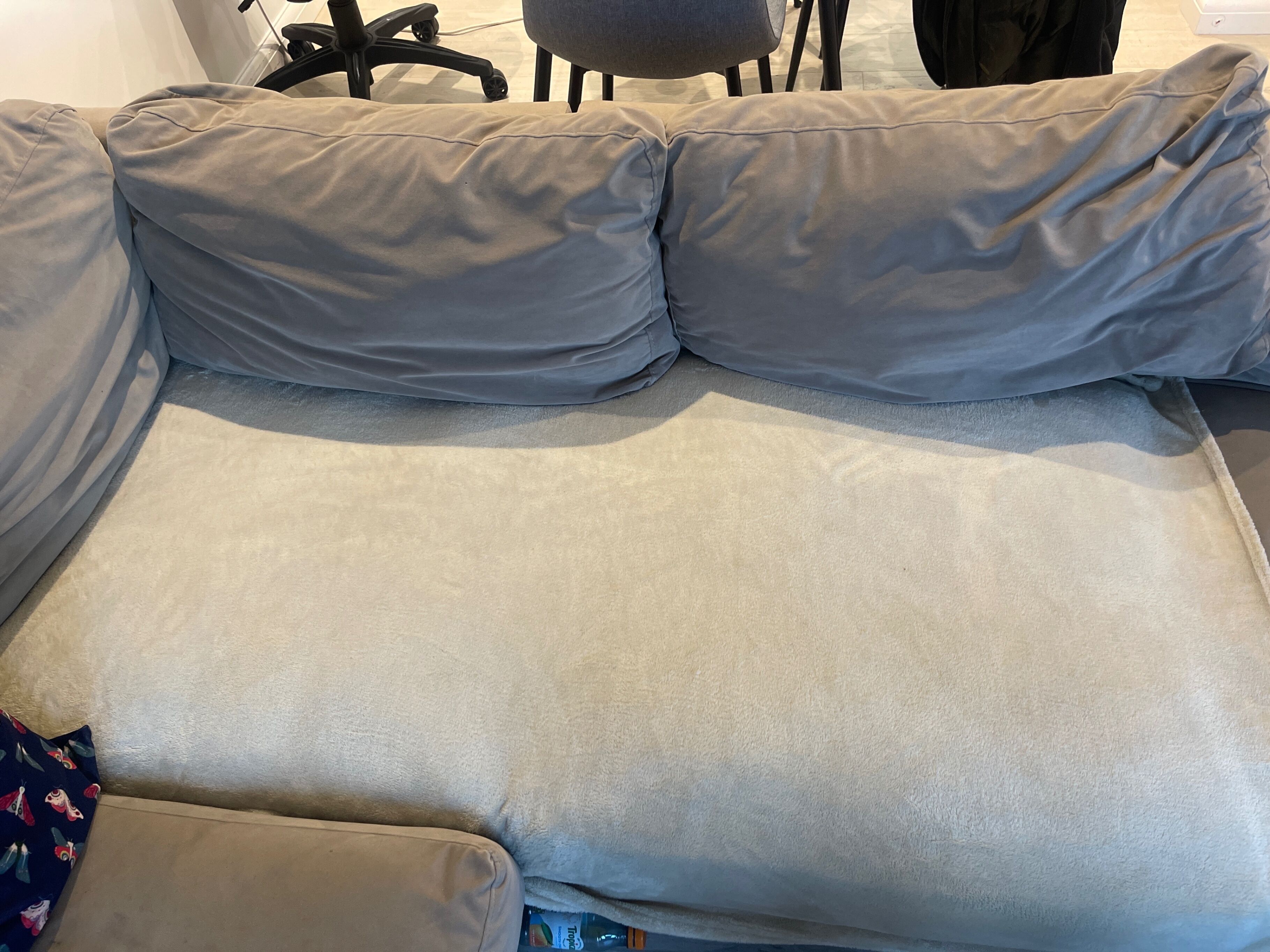 A grey sofa with a light grey cushion, a patterned pillow, and a small blue item on the armrest.