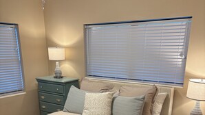 Ein Schlafzimmer mit einem Bett, zwei Nachttischen, einer Kommode und einem Fenster mit Jalousien.