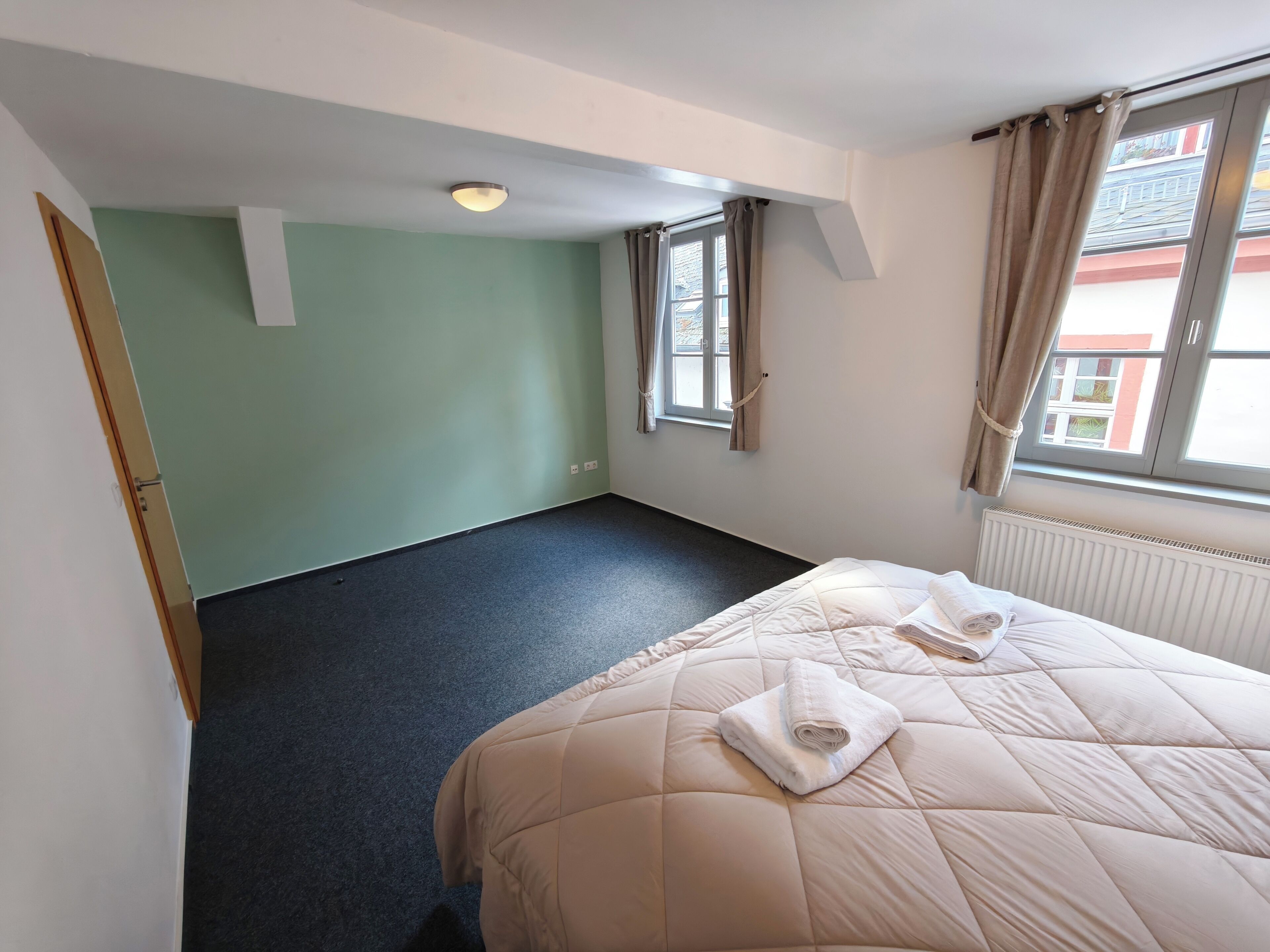 A hotel room with a bed, a window with curtains, a radiator, and a green wall.