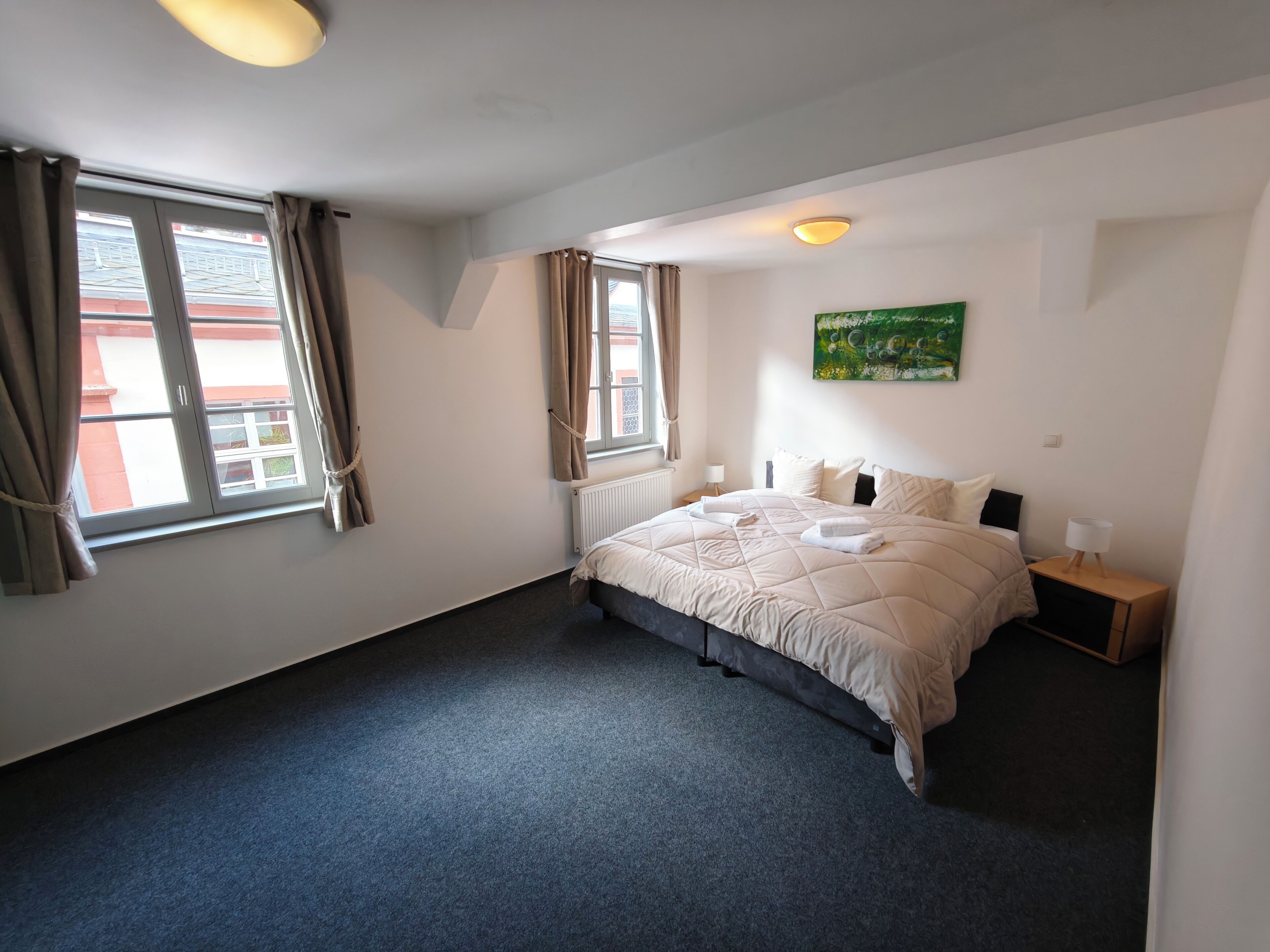 Een slaapkamer met een bed, twee nachtkastjes, een radiator en een raam met gordijnen.