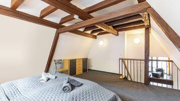 A bedroom with a high ceiling, exposed wooden beams, a bed with a quilt, a wardrobe, and a staircase leading to an upper level.