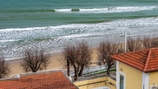 A coastal view with a beach, a yellow building with a red-tiled roof, and leafless trees. - San Menaio Apartment by Rentbeat (Vico del Gargano)