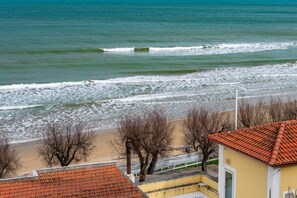 A coastal view with a beach, a yellow building with a red-tiled roof, and leafless trees. - San Menaio Apartment by Rentbeat (Vico del Gargano)
