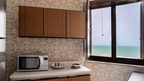 A kitchen with a microwave, cabinets, and a window with a view of the ocean. - San Menaio Apartment by Rentbeat (Vico del Gargano)