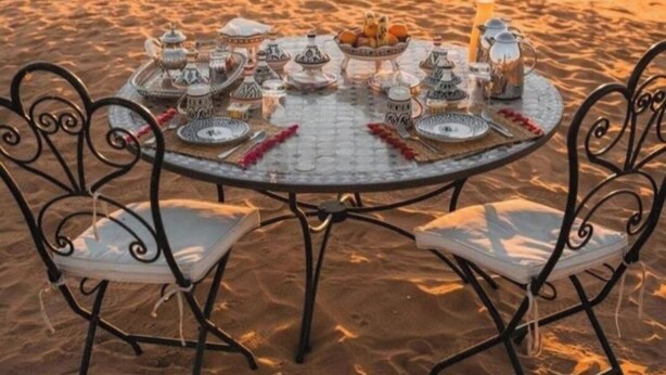 A desert scene with a round table set for a meal, surrounded by desert tents. - Merzouga Luxury Tented (Merzouga)