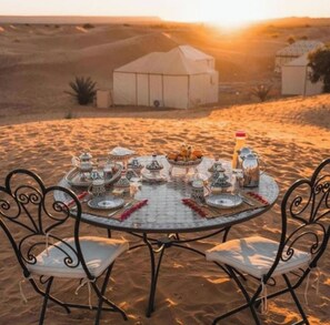 A desert scene with a round table set for a meal, surrounded by desert tents. - Merzouga Luxury Tented (Merzouga)