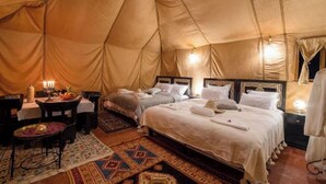 A tented accommodation with two beds, a dining area, and a small table with a lamp. - Merzouga Luxury Tented (Merzouga)