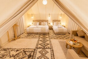 Un alloggio in tenda con due letti, un divano, un tavolo con frutta e tappeti decorati.