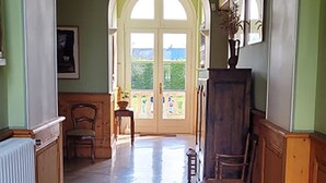 A hallway with a tiled floor, wooden chairs, a radiator, and a large arched doorway leading to an outdoor area. - Le Château de Chambois ✦ Confidential ✦ Families ✦ Seminars (Gouffern en Auge)