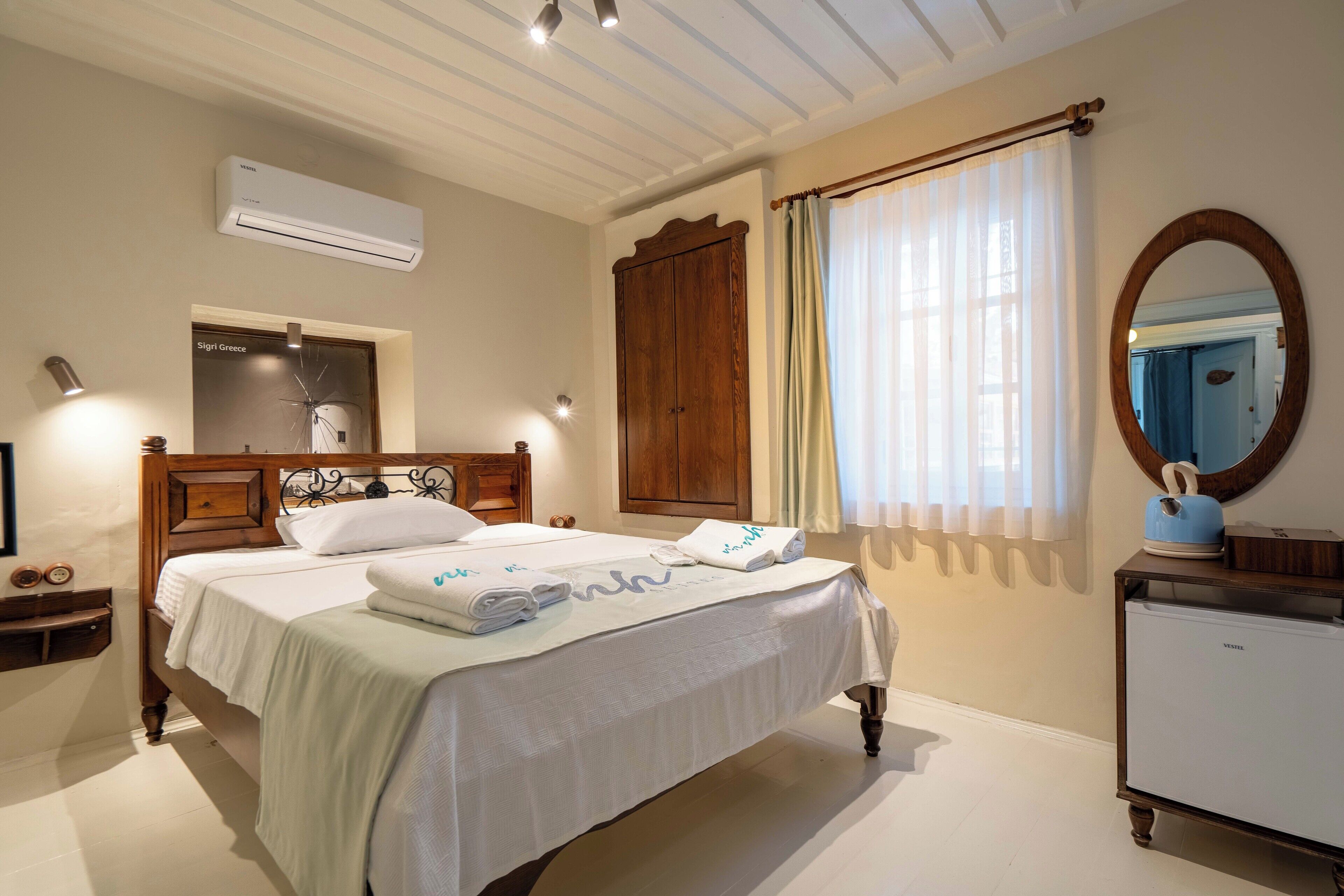 Habitación de hotel con cama, armario, espejo, una pequeña mesa con hervidor y un equipo de aire acondicionado.