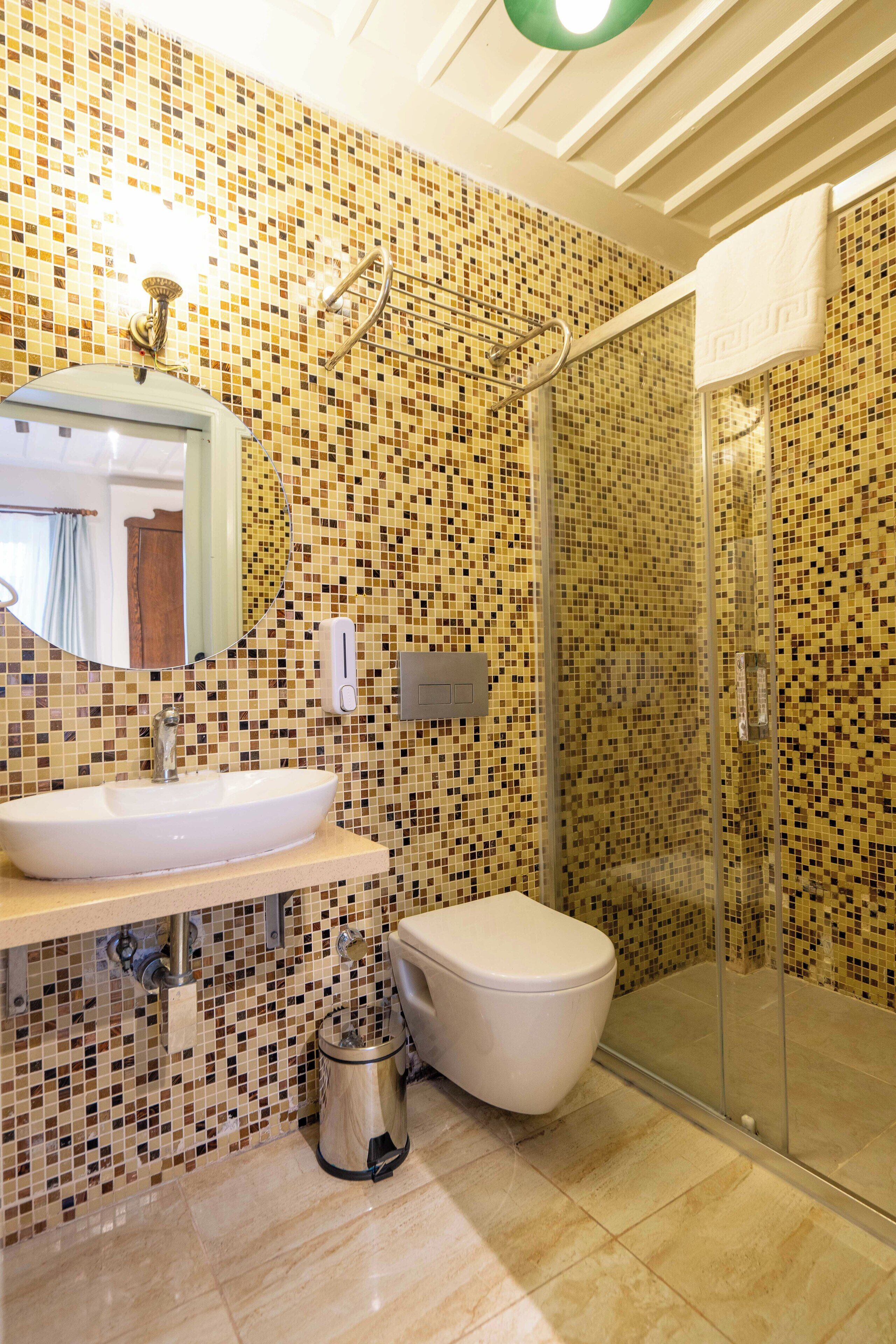 Un baño con pared de mosaicos, lavamanos, inodoro, cabina de ducha de vidrio y espejo.