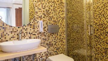 Un baño con pared de mosaicos, lavamanos, inodoro, cabina de ducha de vidrio y espejo.