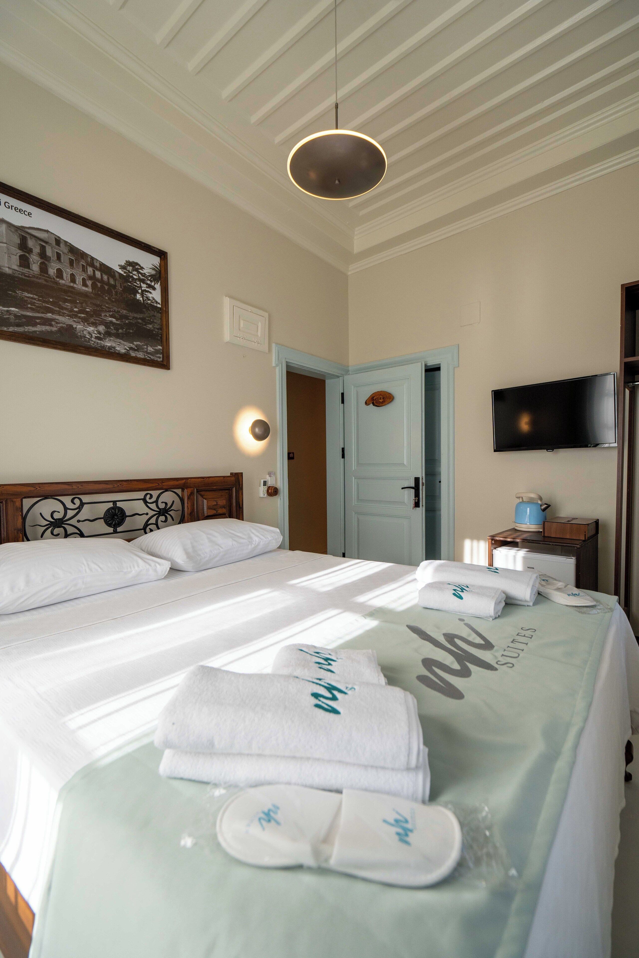 A hotel room with a bed, a television, a door, and a wall-mounted light fixture.