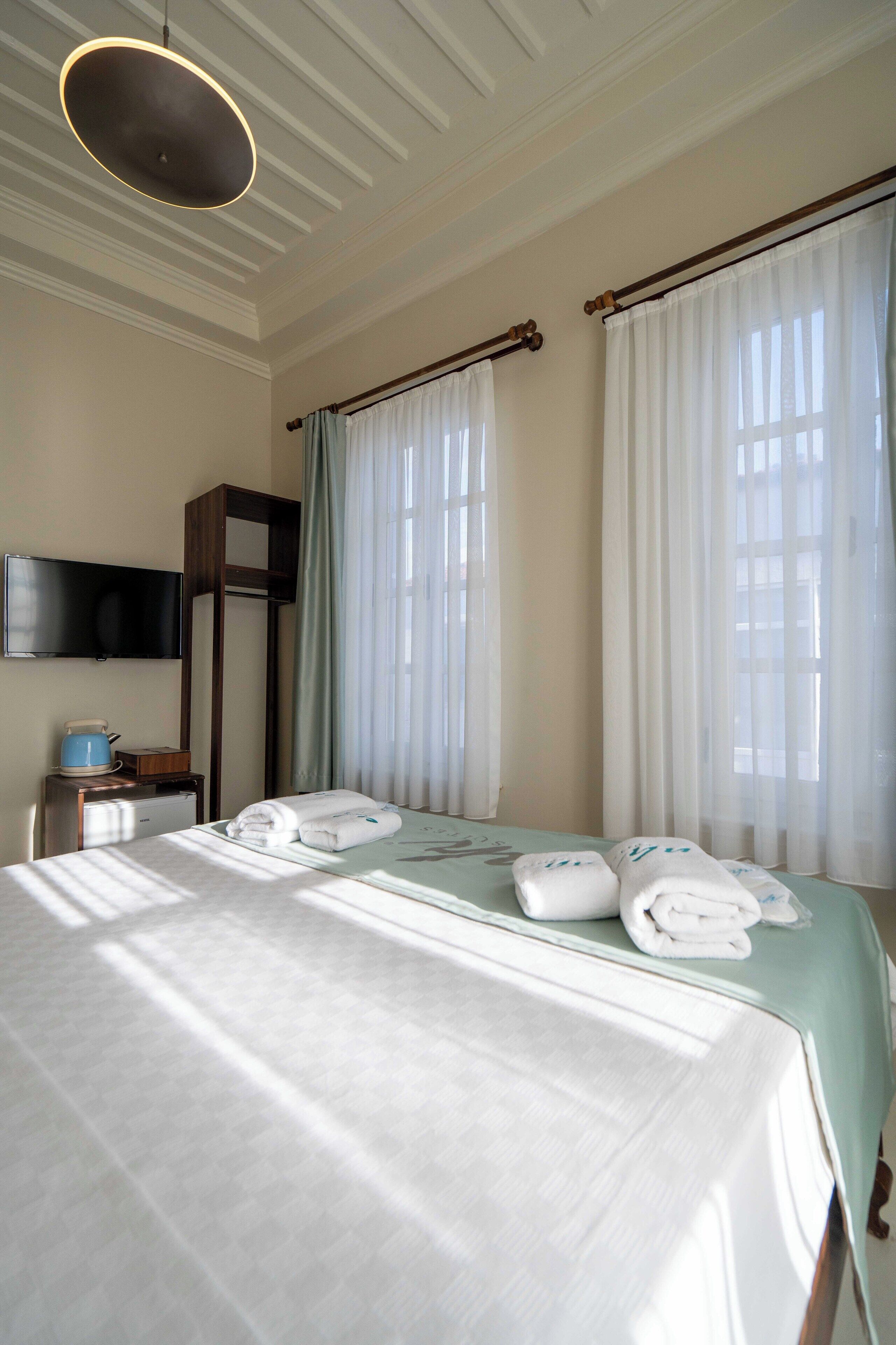 Una habitación de hotel con una cama, un televisor de pantalla plana, un escritorio con cafetera y cortinas en las ventanas.