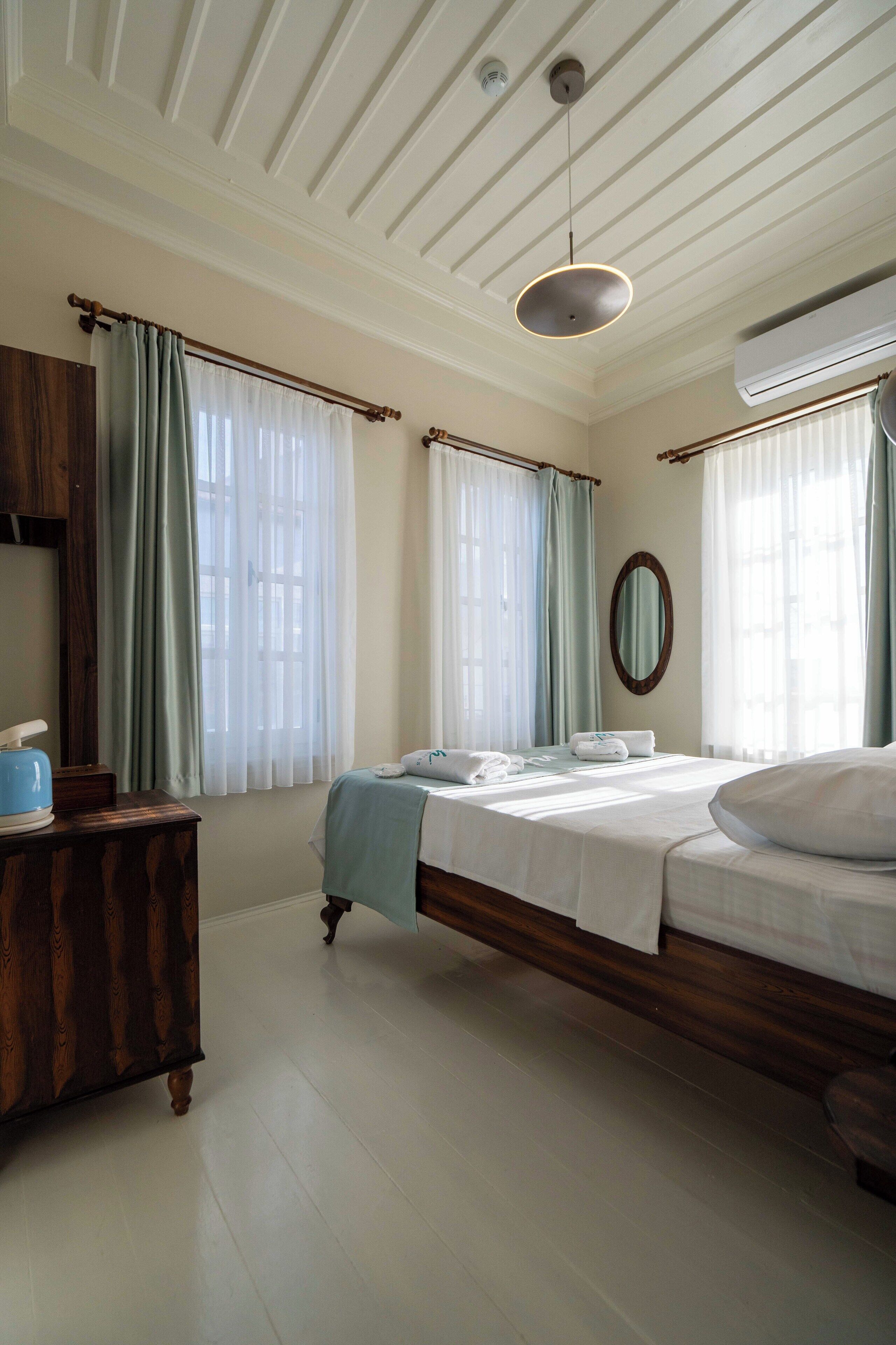 A bedroom with a wooden bed, a bedside table, a hanging light fixture, and a window with curtains.
