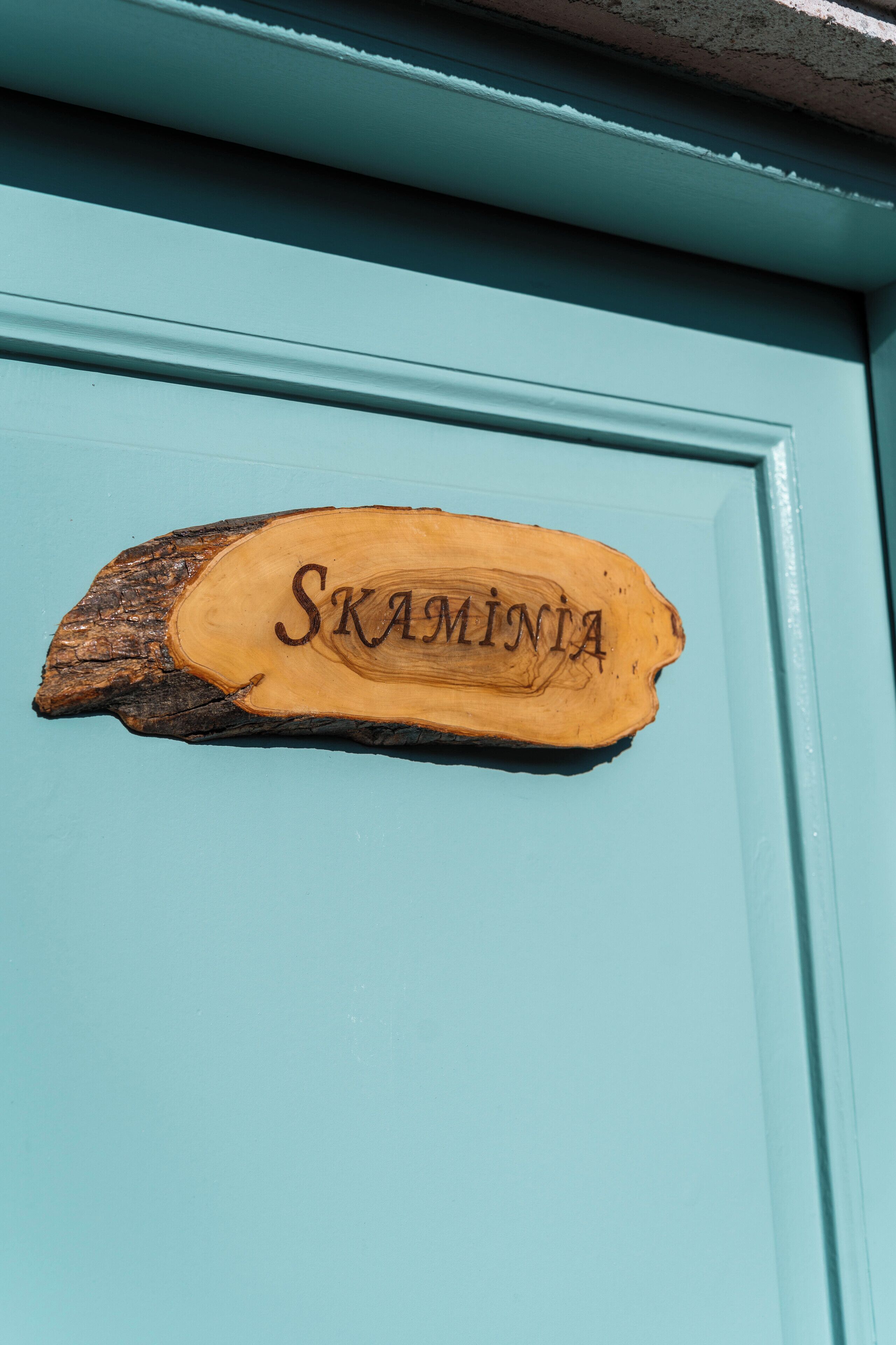 Un letrero de madera con el nombre 'Skamintia' en una puerta color turquesa.