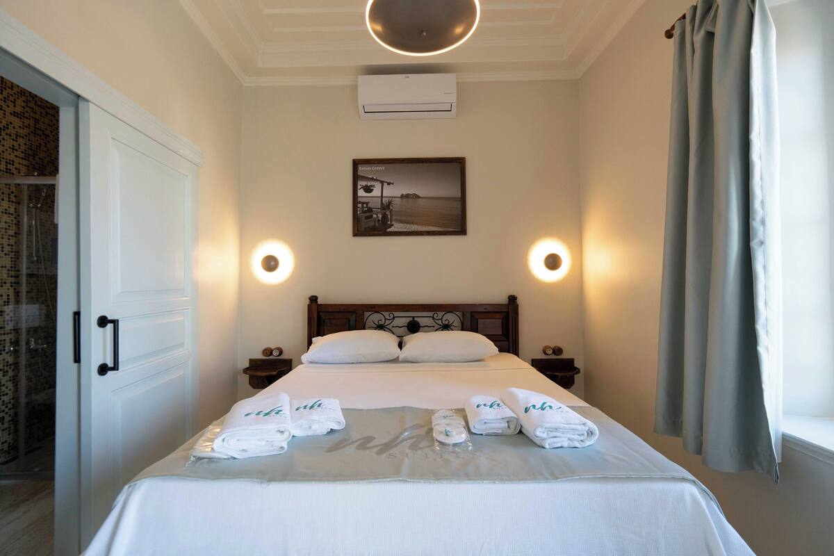 Habitación de hotel con una cama bien hecha, dos mesitas de noche, aire acondicionado de pared y un cuadro enmarcado sobre la cama.