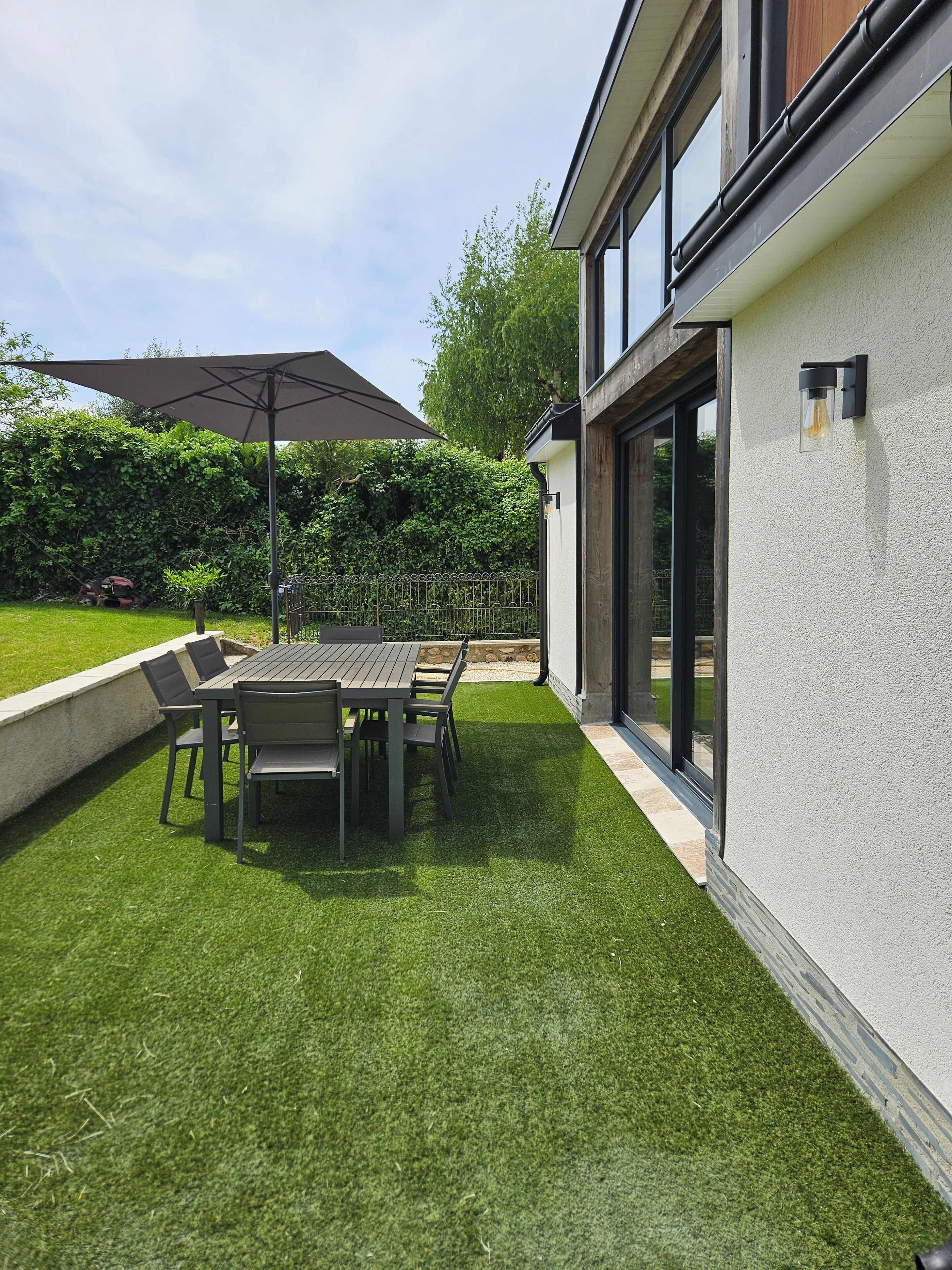 Une terrasse avec une table et des chaises, un grand parasol et une pelouse bien entretenue.