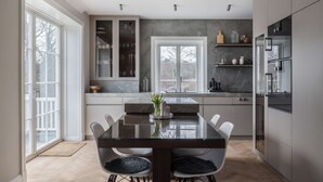 A modern kitchen with a glass dining table, white chairs, and a view through the window. - Villa Strandliv invites you to experience an extraordinary stay in a one-of-a-kind residence. (Gustavsberg)
