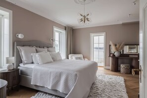 Ein Schlafzimmer mit einem großen Bett, Nachttischen, einer Kommode, einem Spiegel und Blick durch ein Fenster.