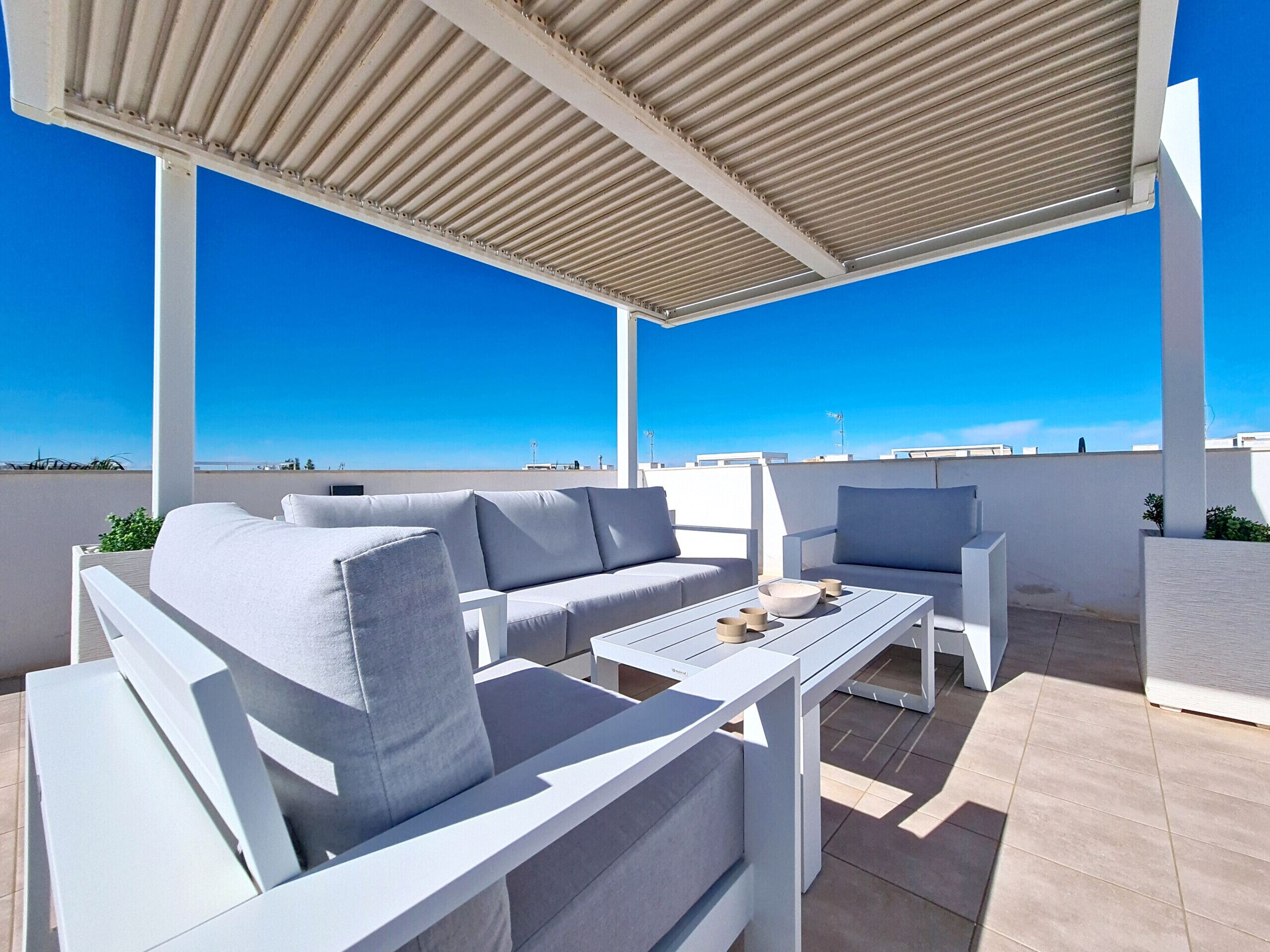 A covered outdoor seating area with white furniture and a clear view of the sky.