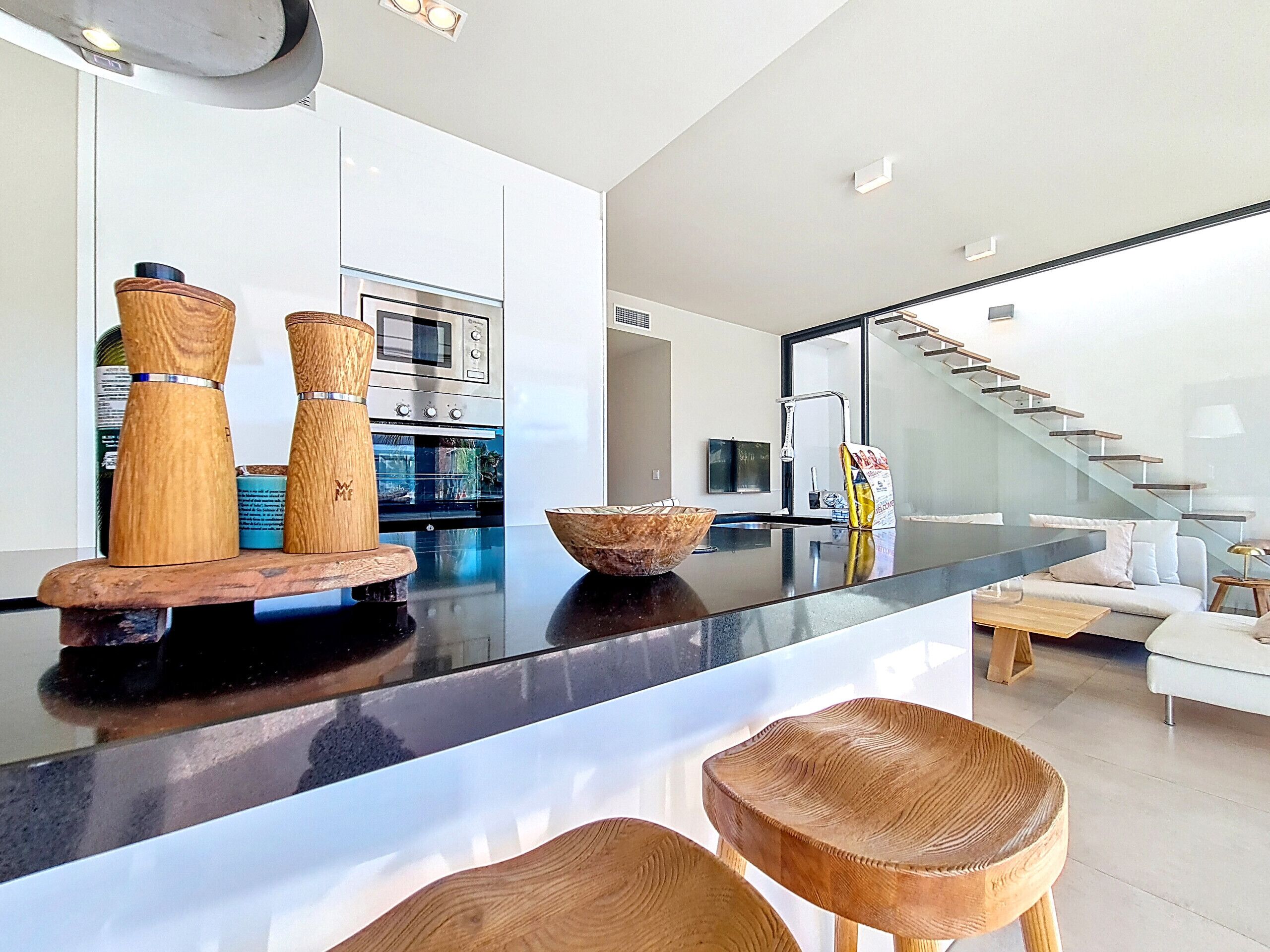A modern kitchen with a black countertop, wooden stools, and a built-in oven.