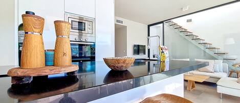 A modern kitchen with a black countertop, wooden stools, and a built-in oven.