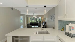 Une cuisine moderne dotée d’un îlot central, d’appareils électroménagers en acier inoxydable et donnant sur la salle à manger.