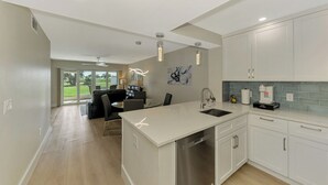 Une cuisine moderne avec des meubles blancs, un îlot central et un coin repas doté de chaises noires.