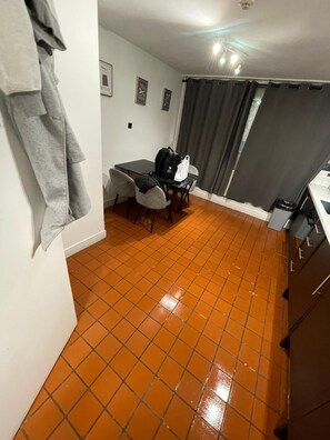 A small dining area with a table and chairs, a grey jacket hanging on the wall, and a tiled floor. - Sleep14 in Victoria London 43VPR (London)
