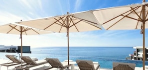 A poolside area with lounge chairs and umbrellas overlooking the sea.