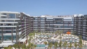 Ein mehrstöckiges Hotel mit Poolbereich auf dem Dach, inklusive Liegestühlen und Sonnenschirmen.