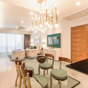 A modern living room with a glass dining table, wooden chairs, a ceiling fan, and a large wooden door.