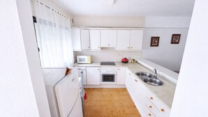 Cozinha compacta com armários brancos, micro-ondas, forno e pia.