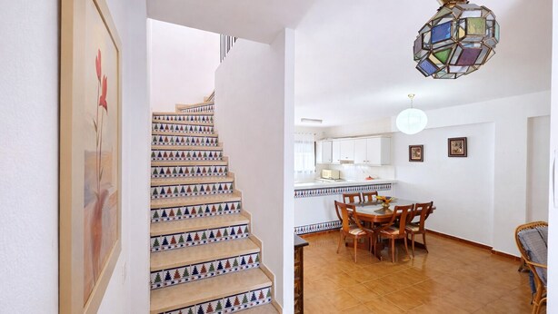 Escada com degraus coloridos que levam a uma sala de jantar com mesa e cadeiras.