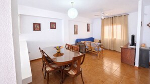 Ampla sala de estar com mesa de jantar, cadeiras, sofá e televisão.