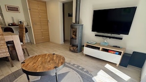 Een woonkamer met een ronde houten salontafel, een televisie, een open haard en een eethoek met stoelen en een tafel.