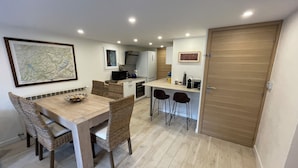 Een kleine keuken met een eethoek, met een houten tafel, rieten stoelen en een klein aanrecht met een magnetron.