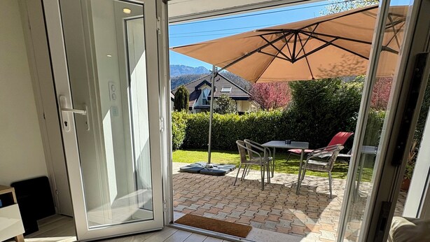 Een kamer met een schuifdeur naar een terras buiten, met een tafel, stoelen en een grote parasol.